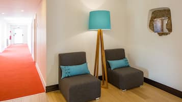 Un pasillo con alfombra roja que conduce a una habitación con dos sillones grises y una lámpara de pie.