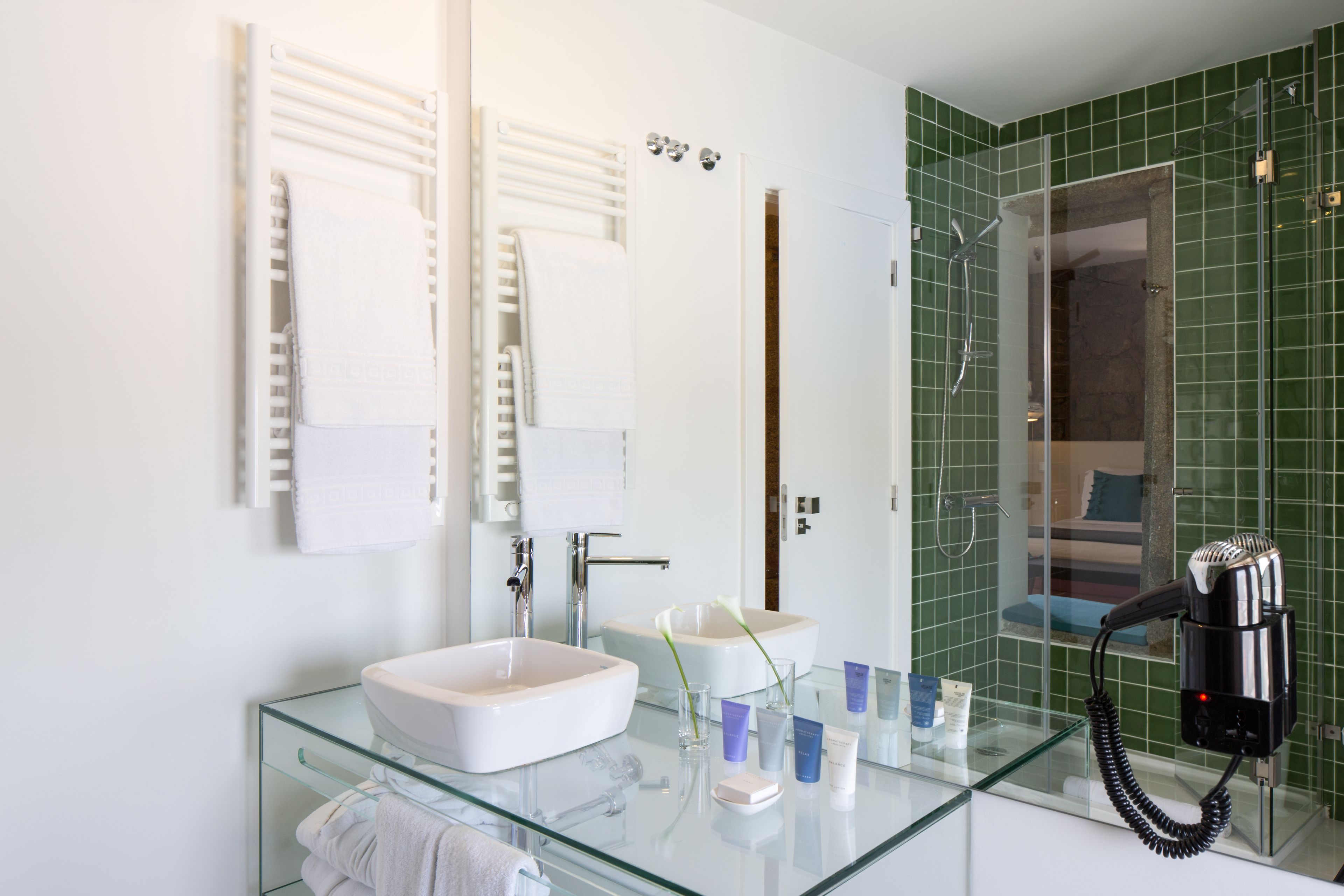 A modern bathroom with a glass sink, white fixtures, and a hairdryer on the counter.