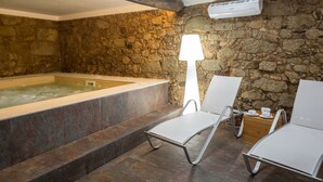 Un área de spa con pared de piedra, bañera de hidromasaje y dos sillones blancos.