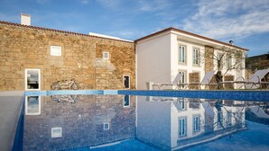 Una piscina con un muro de piedra y un edificio blanco con techo de tejas.
