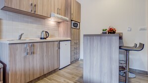 A modern kitchen with wooden cabinets, a built-in microwave, a kettle, and a small bar area with stools. - Adriatik Budva apartments (Budva)