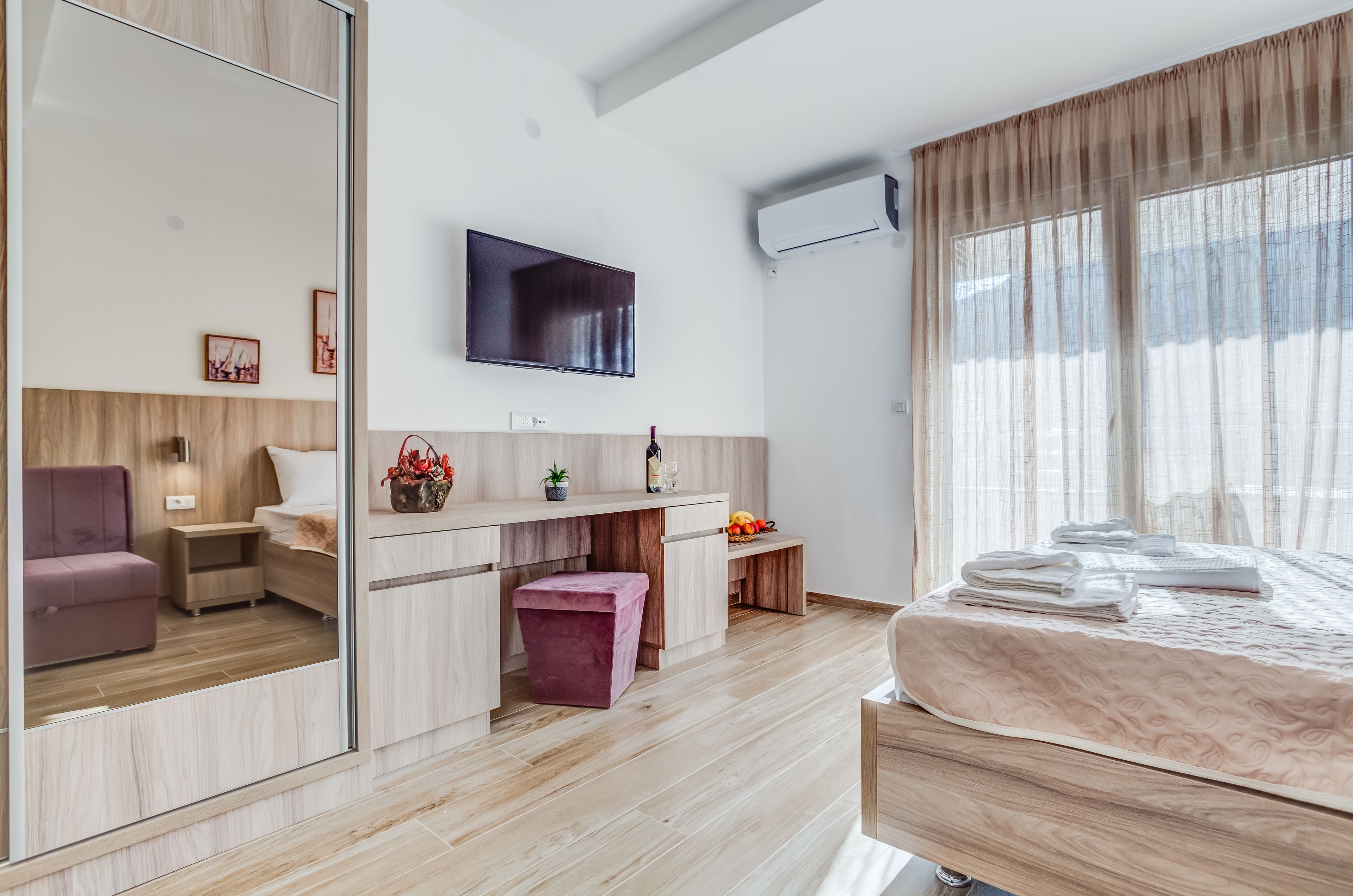 Een moderne hotelkamer met een groot bed, een flatscreen-tv, een bureau met stoel, een zithoek en een groot raam met gordijnen.