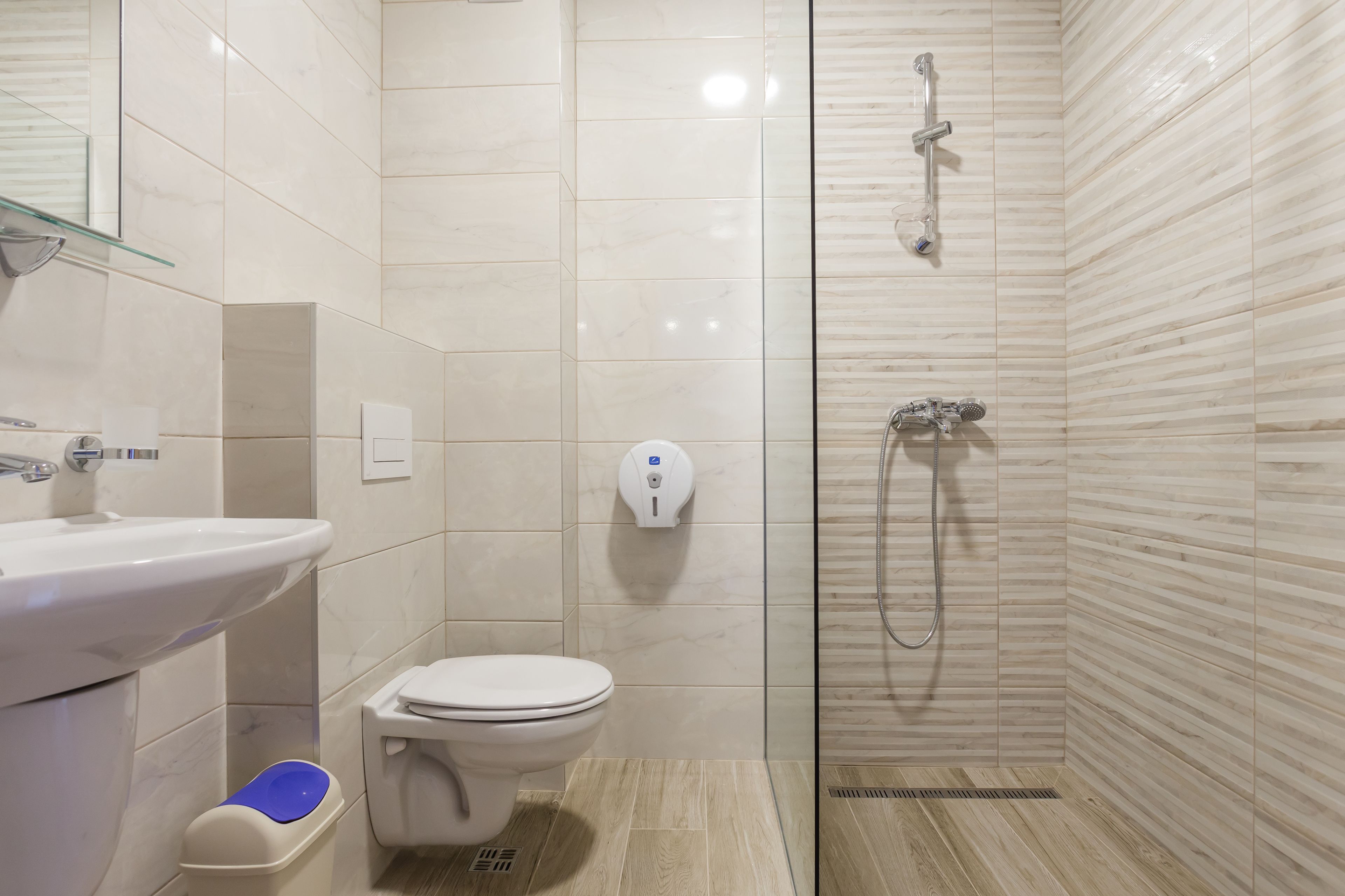 Een moderne badkamer met een glazen douchecabine, een witte wastafel en een toilet.