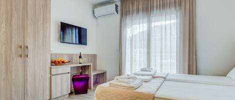 A modern hotel room with a large bed, a flat-screen TV, a minibar, and a large window with curtains.