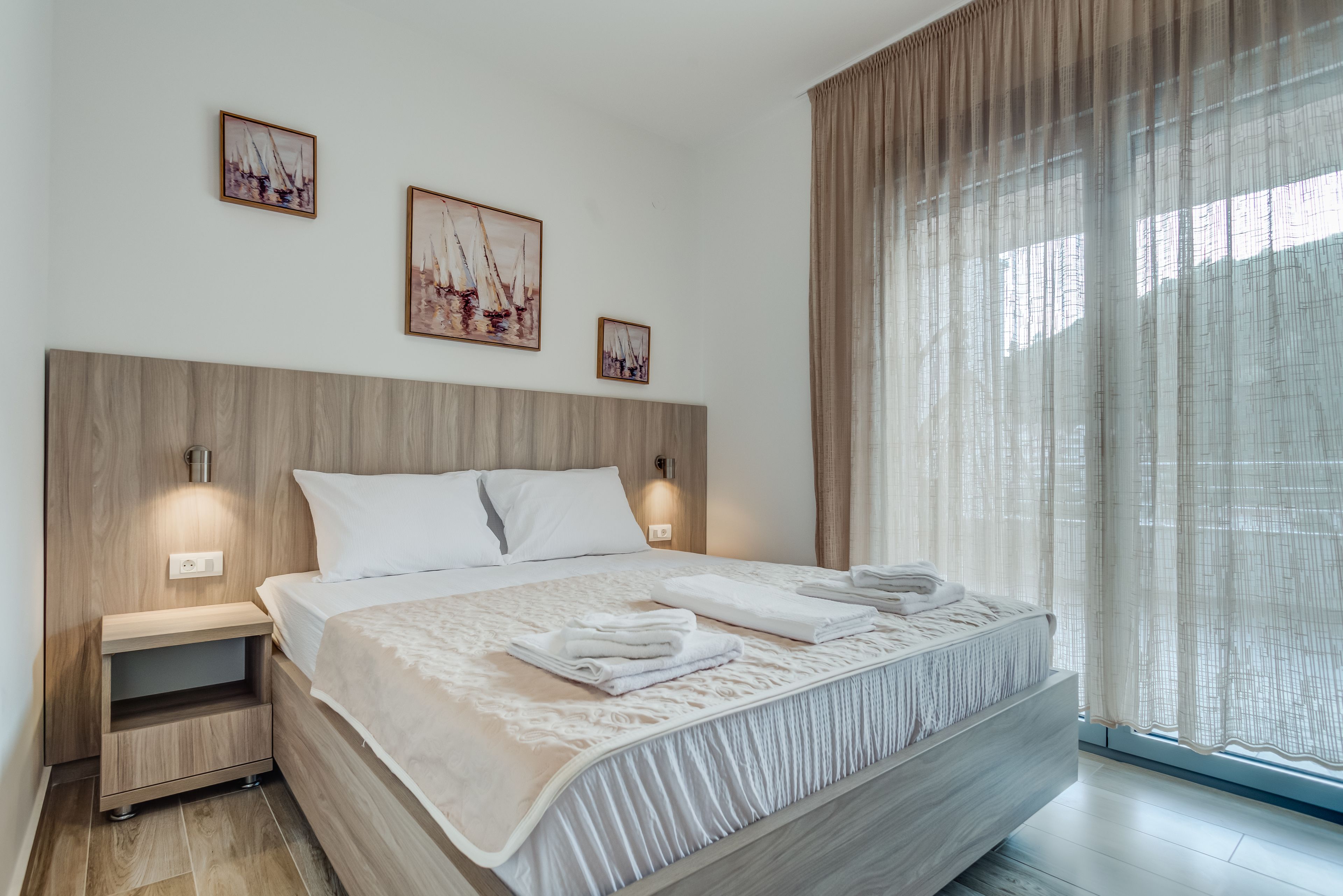 A modern hotel room with a large bed, wooden headboard, and artwork on the walls.