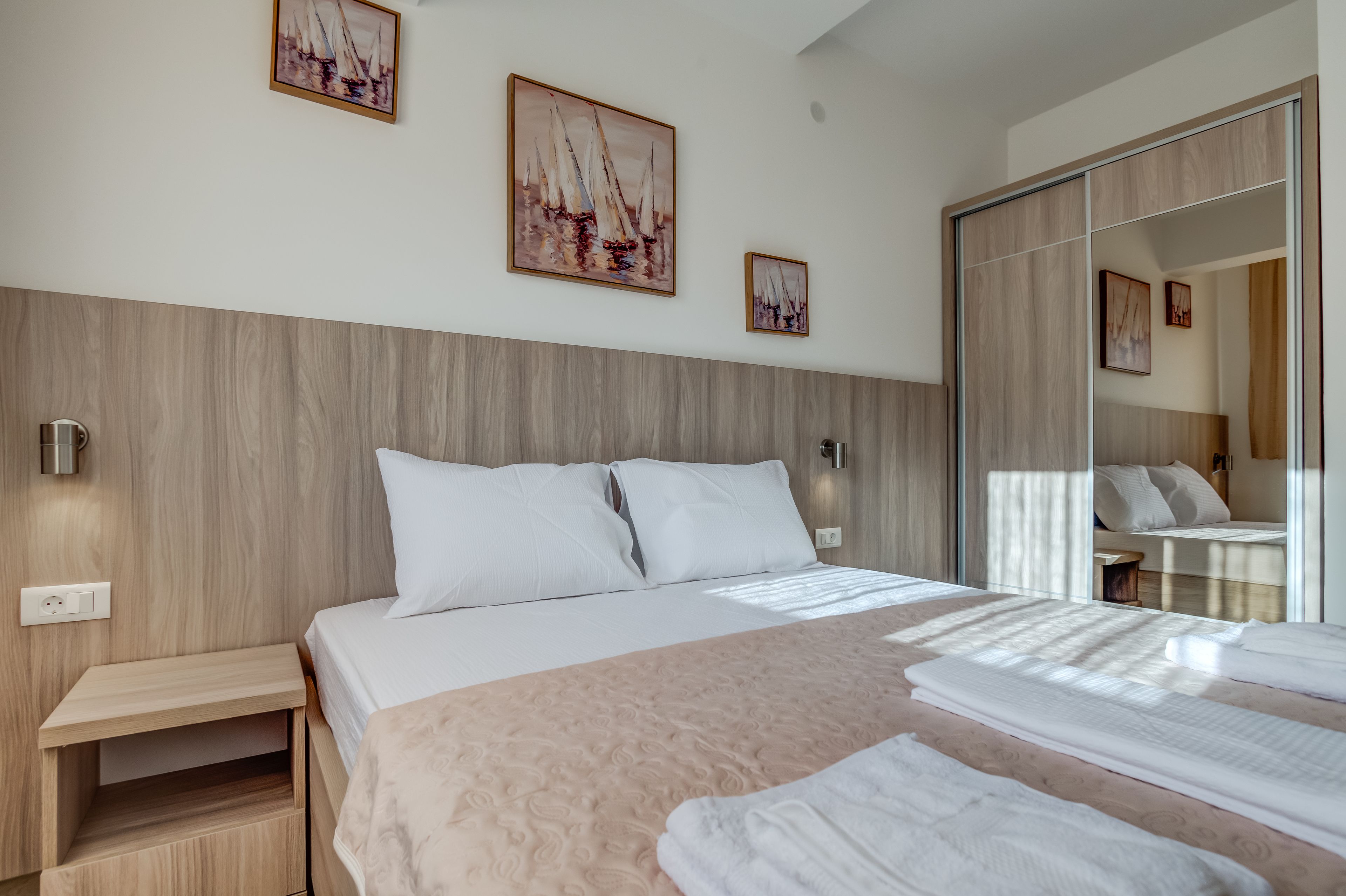A modern hotel room with a large bed, wooden headboard, and a wardrobe with a mirror.