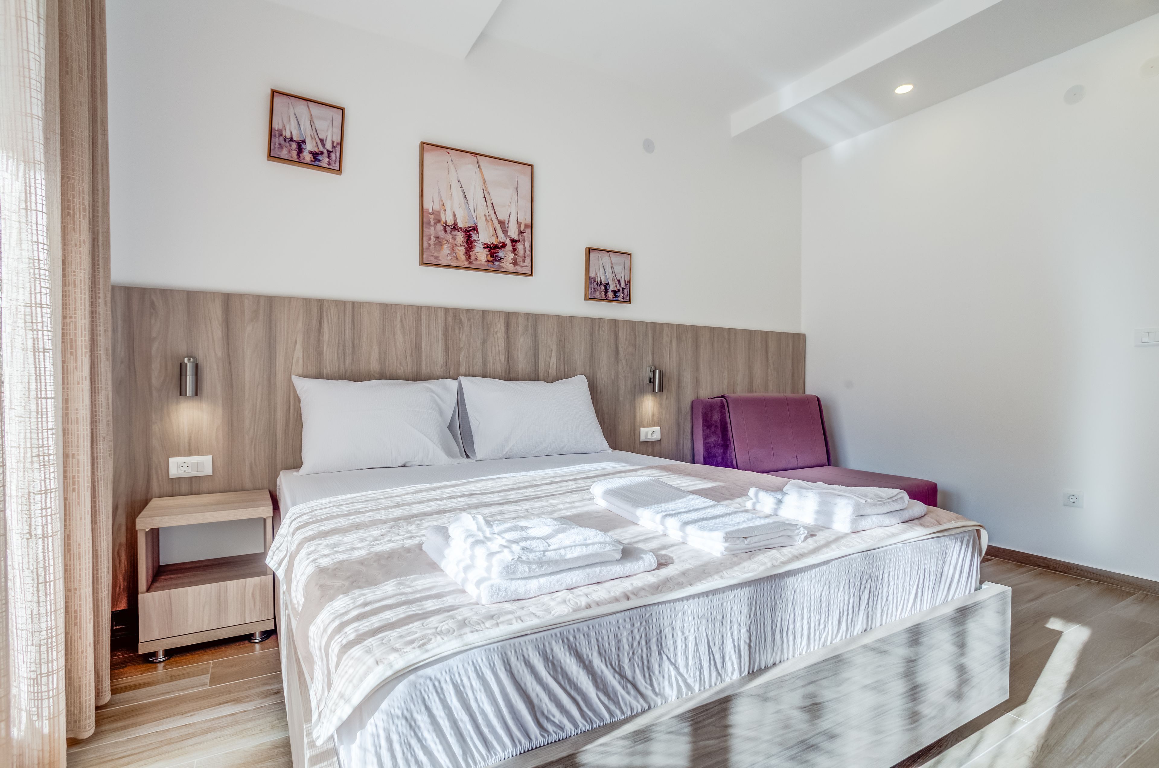 Ein modernes Hotelzimmer mit einem großen Bett, einem Holzkopfende, zwei Nachttischen, einem violetten Sessel und zwei Wandlampen.