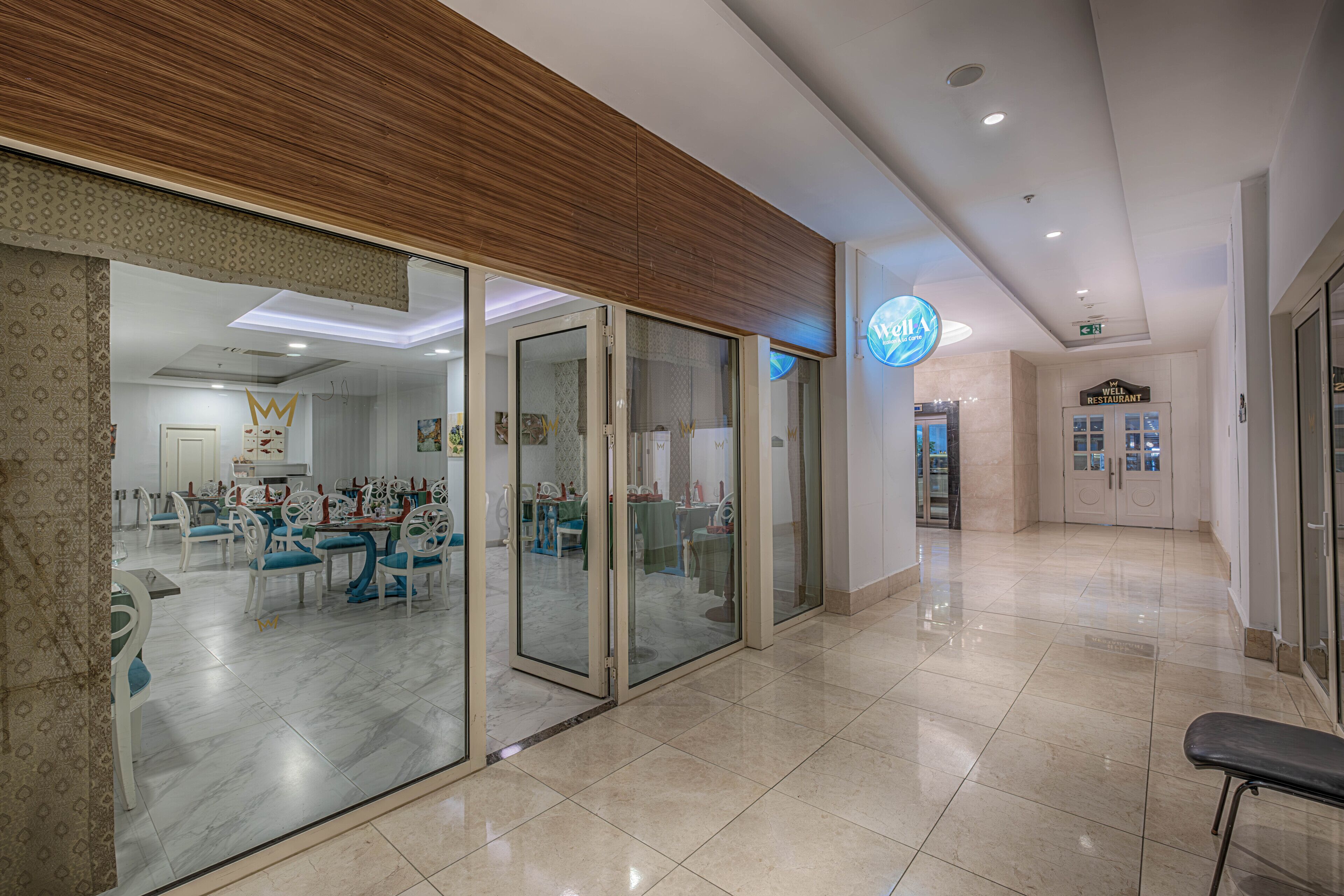 A modern hotel lobby with a dining area, a reception desk, and a sign for a well-known restaurant.