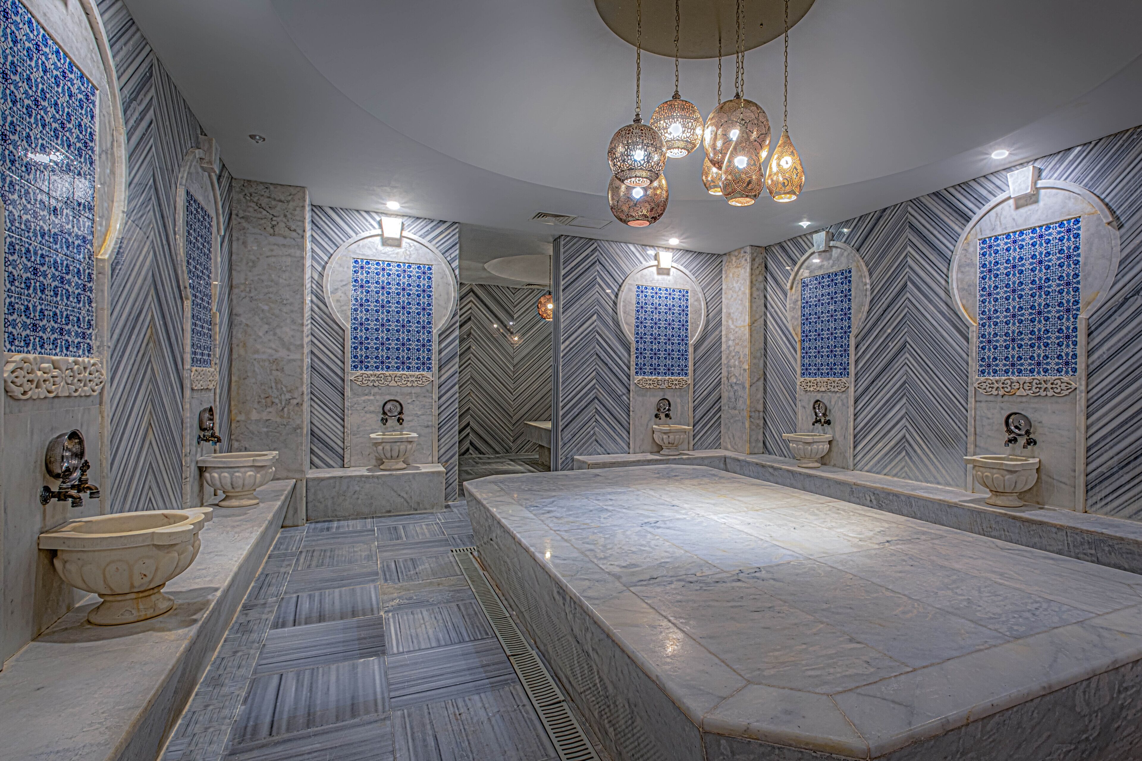 Un baño lujoso con un lavamanos grande de mármol, varios espejos e iluminación decorativa.