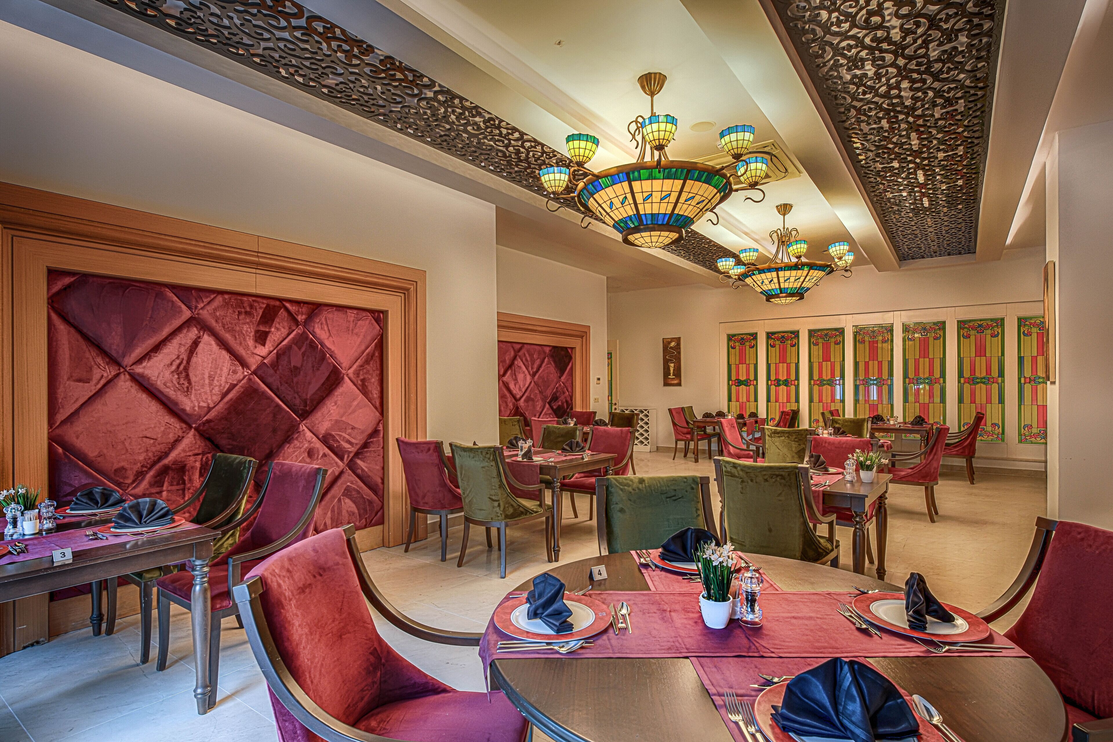 A dining area with multiple tables and chairs, a decorative ceiling, and a patterned wall.