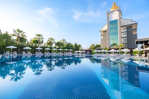 Una piscina con sillas de descanso y sombrillas, rodeada de palmeras y un edificio de hotel.