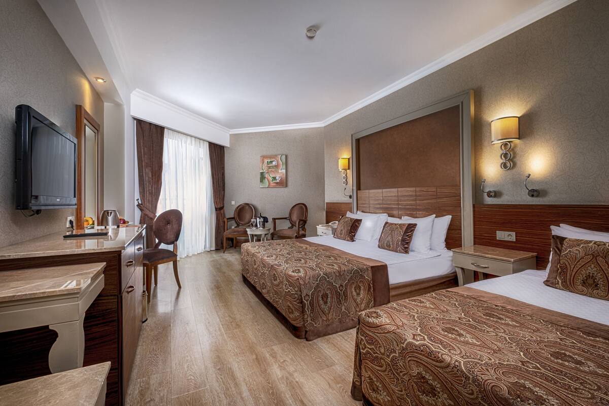 A hotel room with two beds, a desk, a chair, a television, and a painting on the wall.
