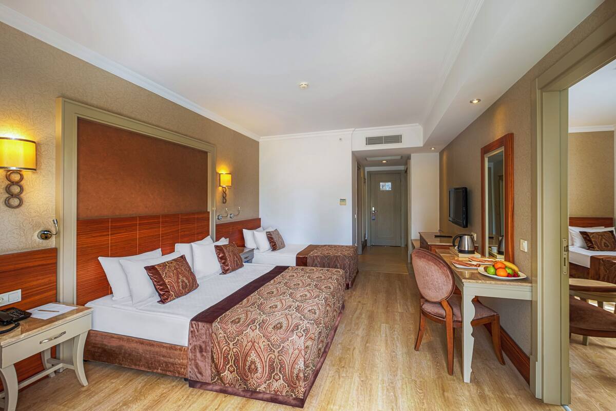 A hotel room with a large bed, a desk, and a chair. There is a television on the desk and a mirror on the wall.