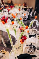Una mesa de comedor decorada con cristalería transparente, servilletas blancas y tulipanes anaranjados en jarrones.