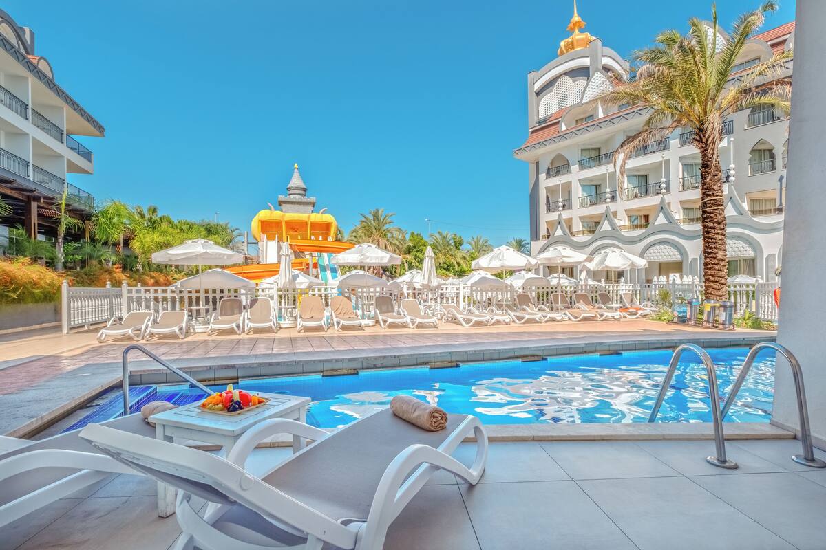 A poolside area with lounge chairs, a table with fruit, and a view of a hotel with a distinctive yellow dome and white balconies.
