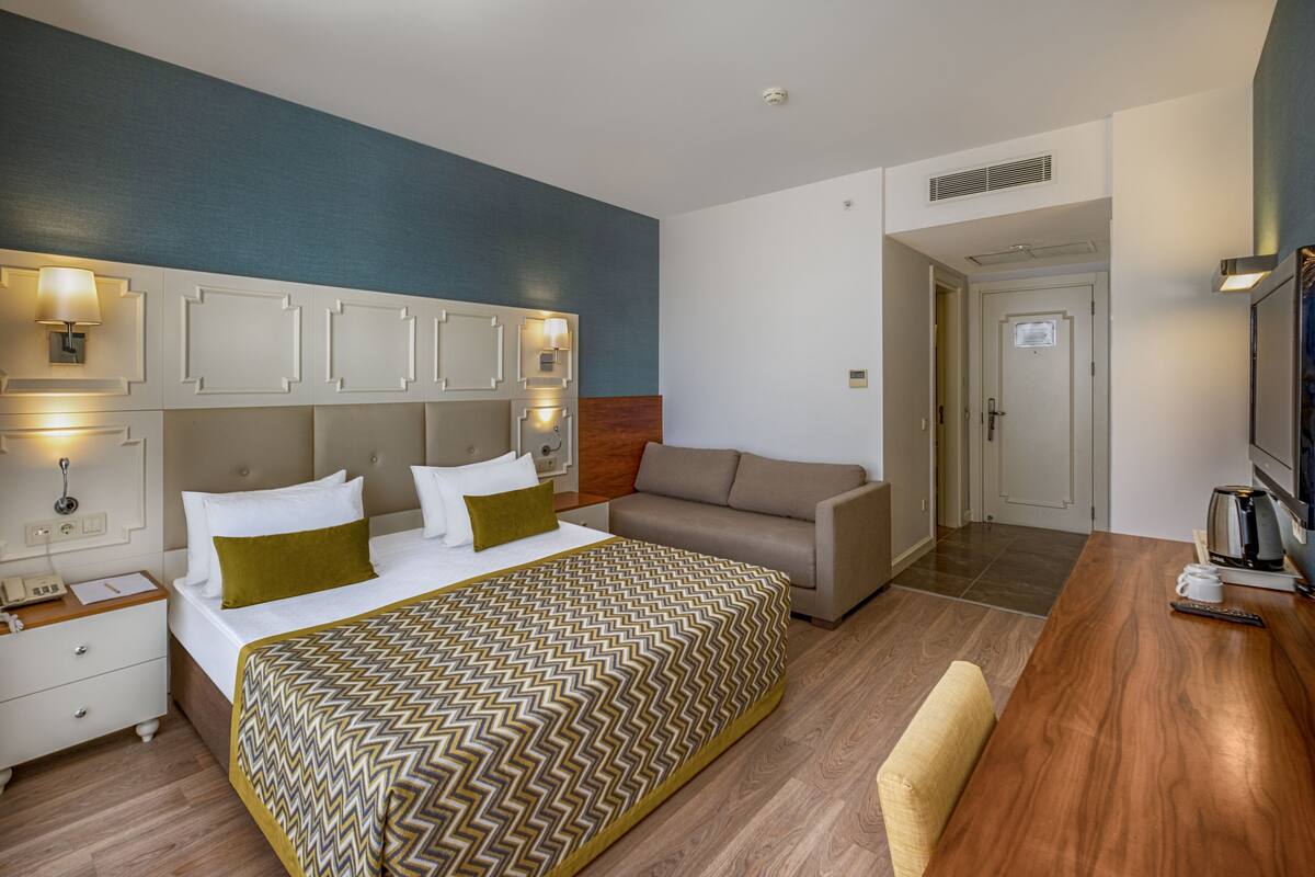 A hotel room with a bed, a sofa, a wooden table, and a TV.