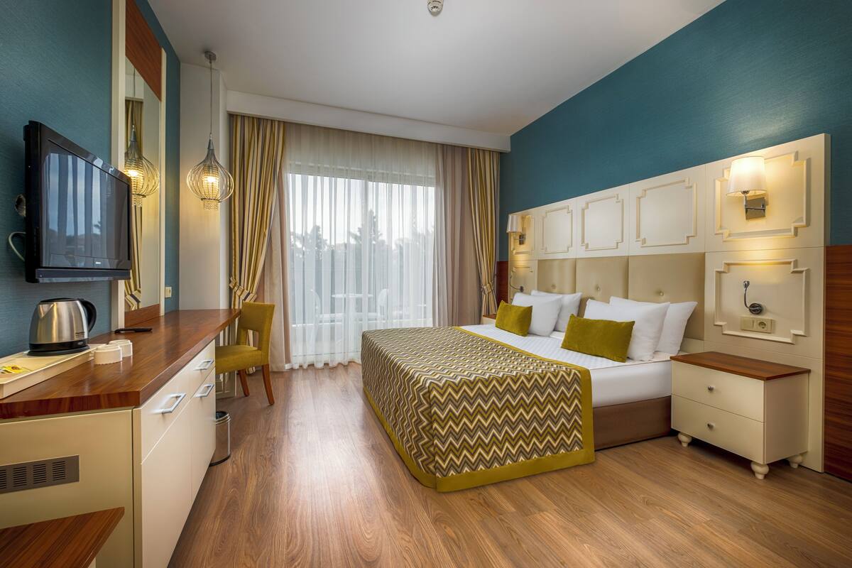 A hotel room with a bed, bedside tables, a desk with a television, and a window with curtains.