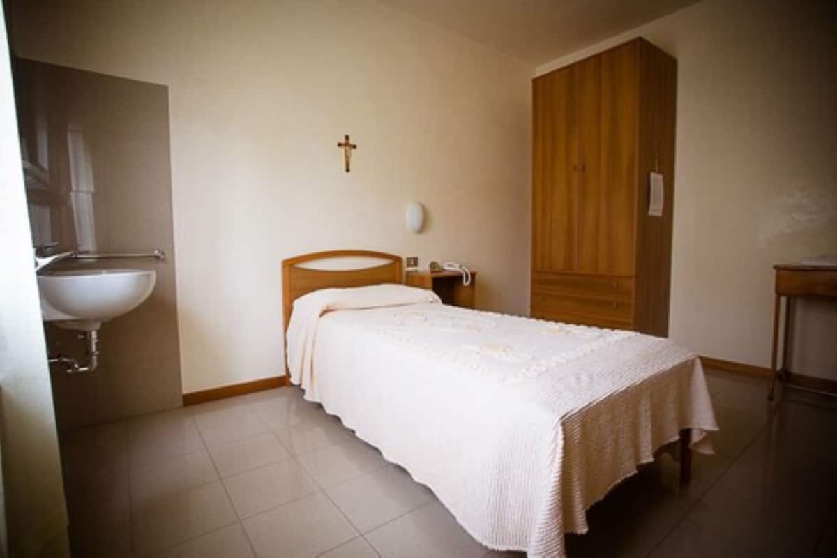 A bedroom with a bed, a wooden wardrobe, a bedside table, and a wall-mounted cross.