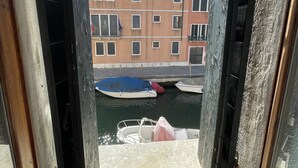 A view through a window of a building with a canal and boats. - Casa Caburlotto (Venice)