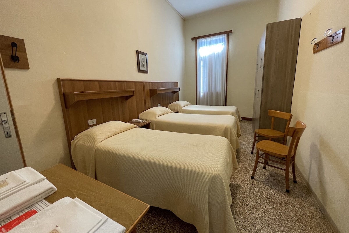 A hotel room with two beds, a wooden headboard, a desk with a telephone, a chair, and a window with curtains.