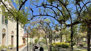 An outdoor seating area with tables and chairs under a pergola, surrounded by greenery and a building with arched windows. - Casa Caburlotto (Venice)