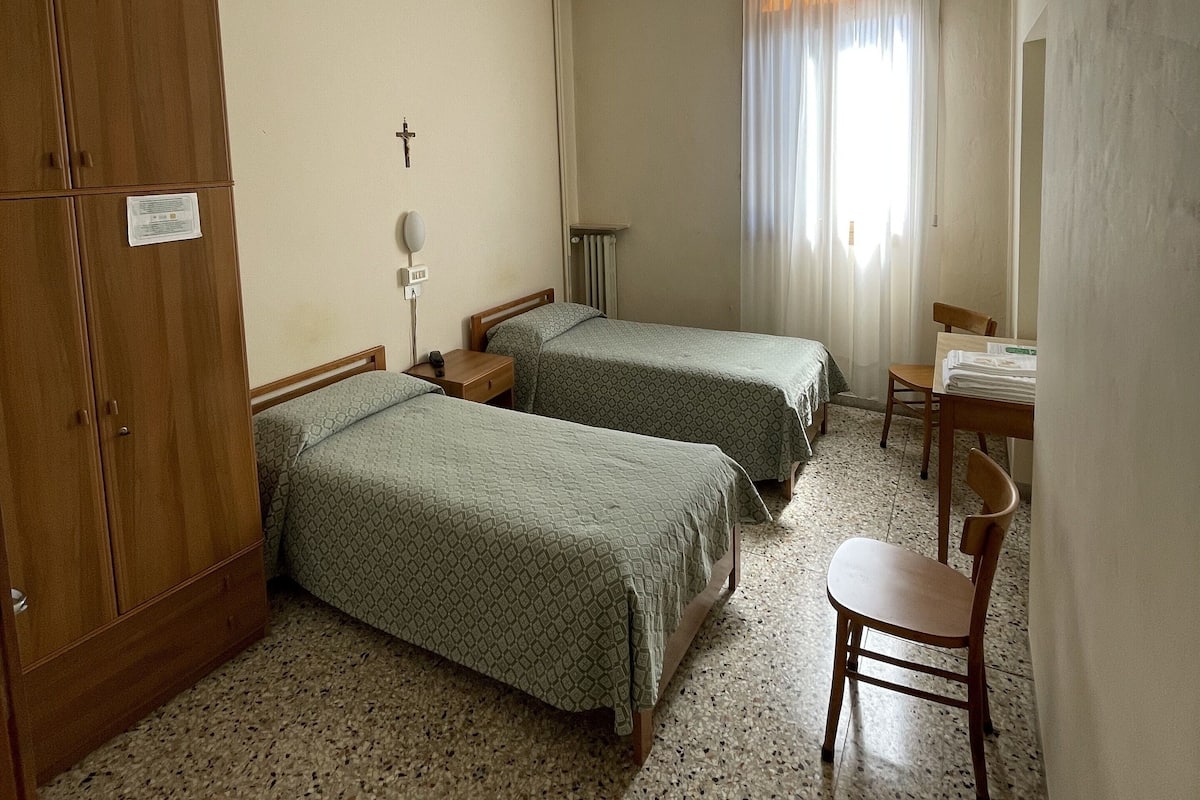 A room with two beds, a wooden wardrobe, a desk, and a chair.