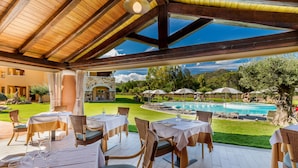 An outdoor dining area with tables and chairs, a pool, and a view of the surrounding landscape. - Hotel Marana (Golfo Aranci)