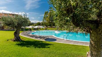 Una piscina con cubierta de madera, rodeada de césped verde y árboles.