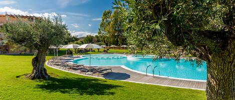 A swimming pool with a wooden deck, surrounded by green grass and trees.