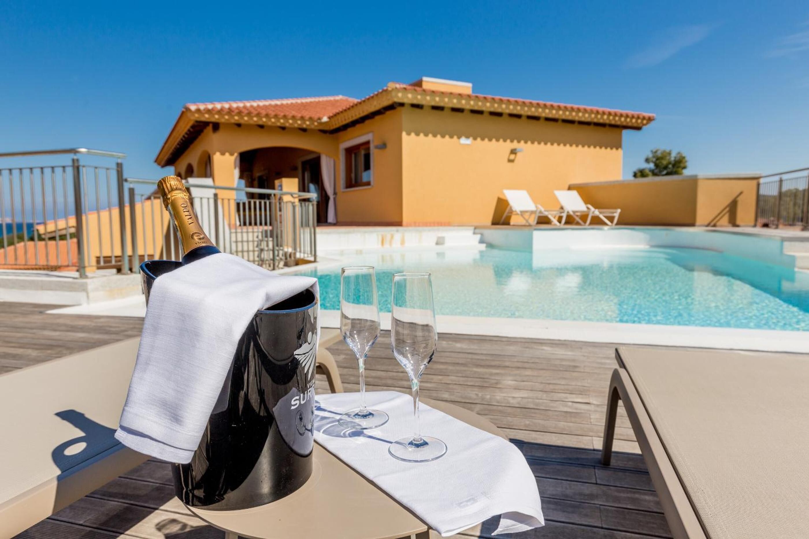 A poolside area with a bottle of champagne, two glasses, and a towel on a table.