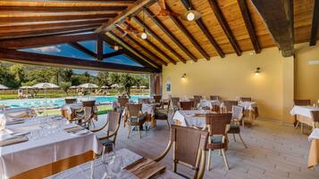 Un espace de restauration en plein air avec des tables et des chaises, une piscine en arrière-plan et une structure de plafond en bois.