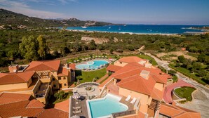 A resort with multiple swimming pools, a beach view, and a mountainous backdrop. - Hotel Marana (Golfo Aranci)