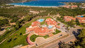 An aerial view of a coastal resort with a swimming pool, multiple buildings, and a beach. - Hotel Marana (Golfo Aranci)