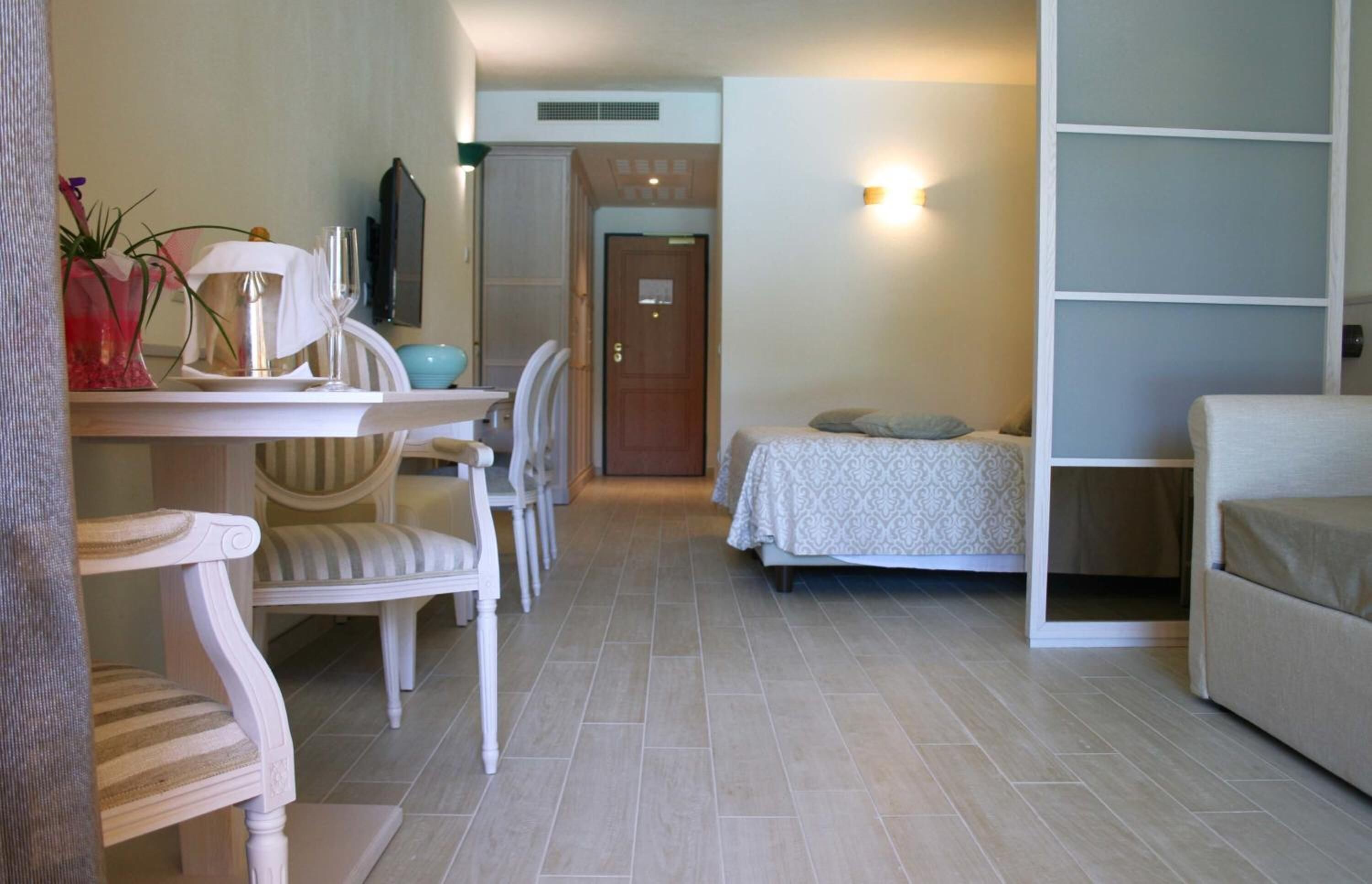 A hotel room with a bed, a sofa, a dining table with chairs, and a small kitchen area.
