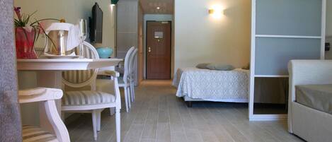 A hotel room with a bed, a sofa, a dining table with chairs, and a small kitchen area.