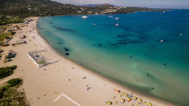 An aerial view of a beach with clear turquoise waters, a sandy shore, and a few boats. - Hotel Marana (Golfo Aranci)