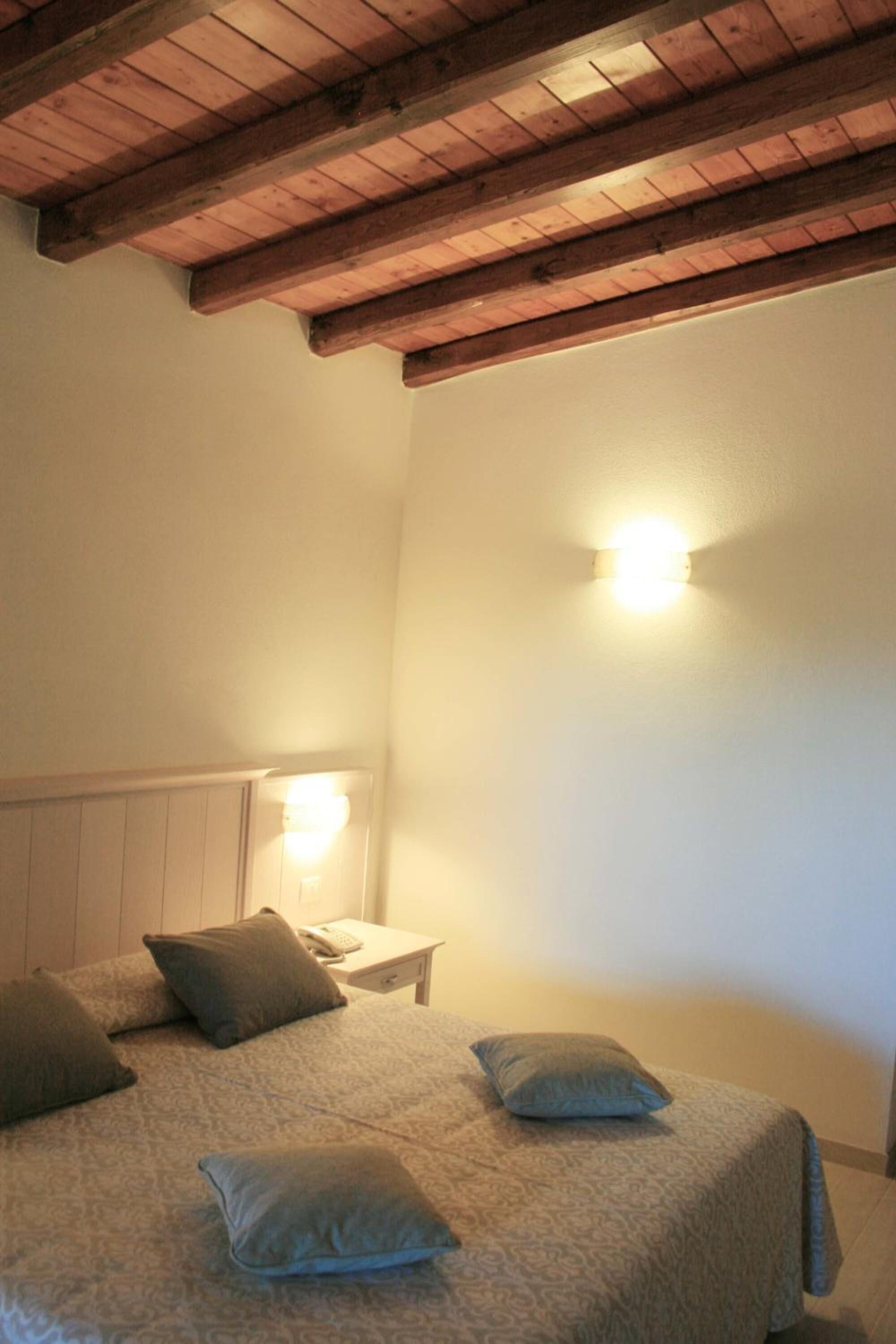Et soveværelse med træloft, seng med mønstret sengetøj og en sengebordlampe.