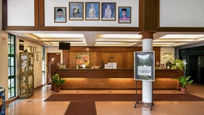 A hotel reception area with a wooden reception desk, framed portraits on the wall, and a signboard.
