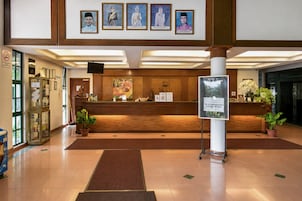 Zona de recepción de un hotel con un mostrador de madera, retratos enmarcados en la pared y un cartel.