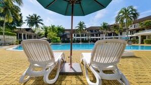 Two white lounge chairs facing a pool with a palm tree and a building in the background. - Sunday Kuantan Near Cherating Beach Formerly Residence Inn (Cherating)