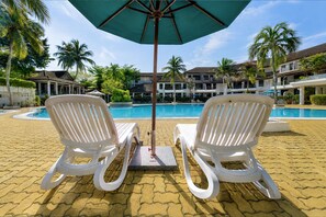Two white lounge chairs facing a pool with a palm tree and a building in the background. - Sunday Kuantan Near Cherating Beach Formerly Residence Inn (Cherating)