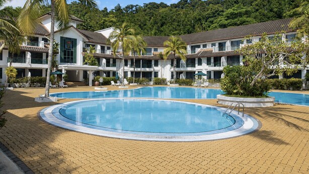 A resort with two swimming pools, palm trees, and a hillside backdrop.