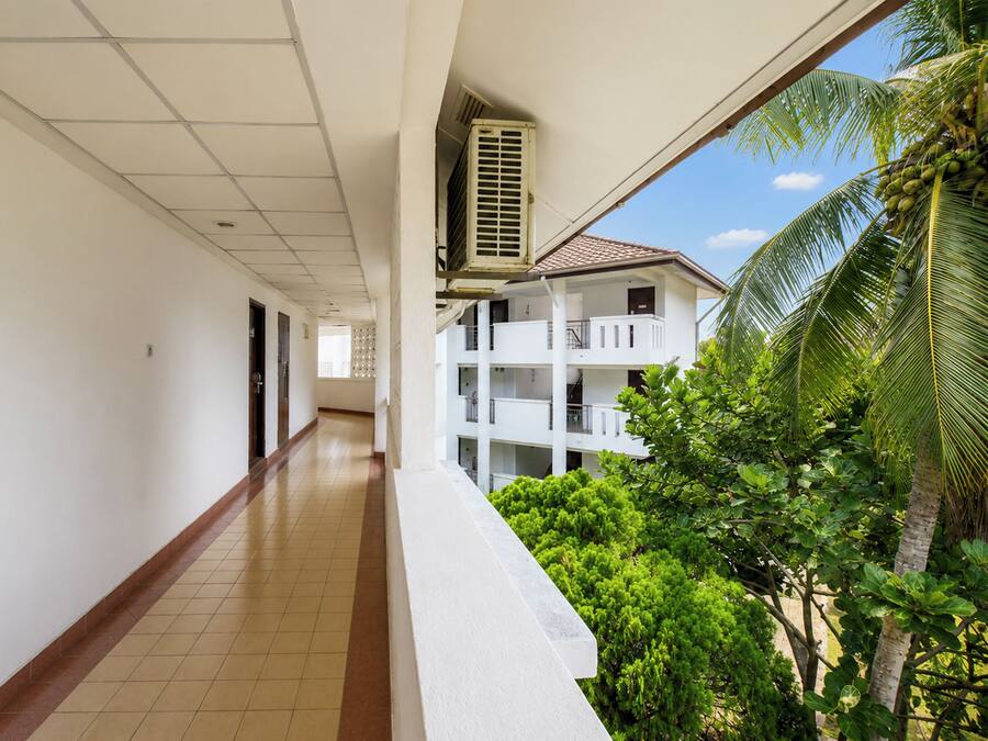 A corridor with a tiled floor, white walls, and a view of a building with balconies and greenery.