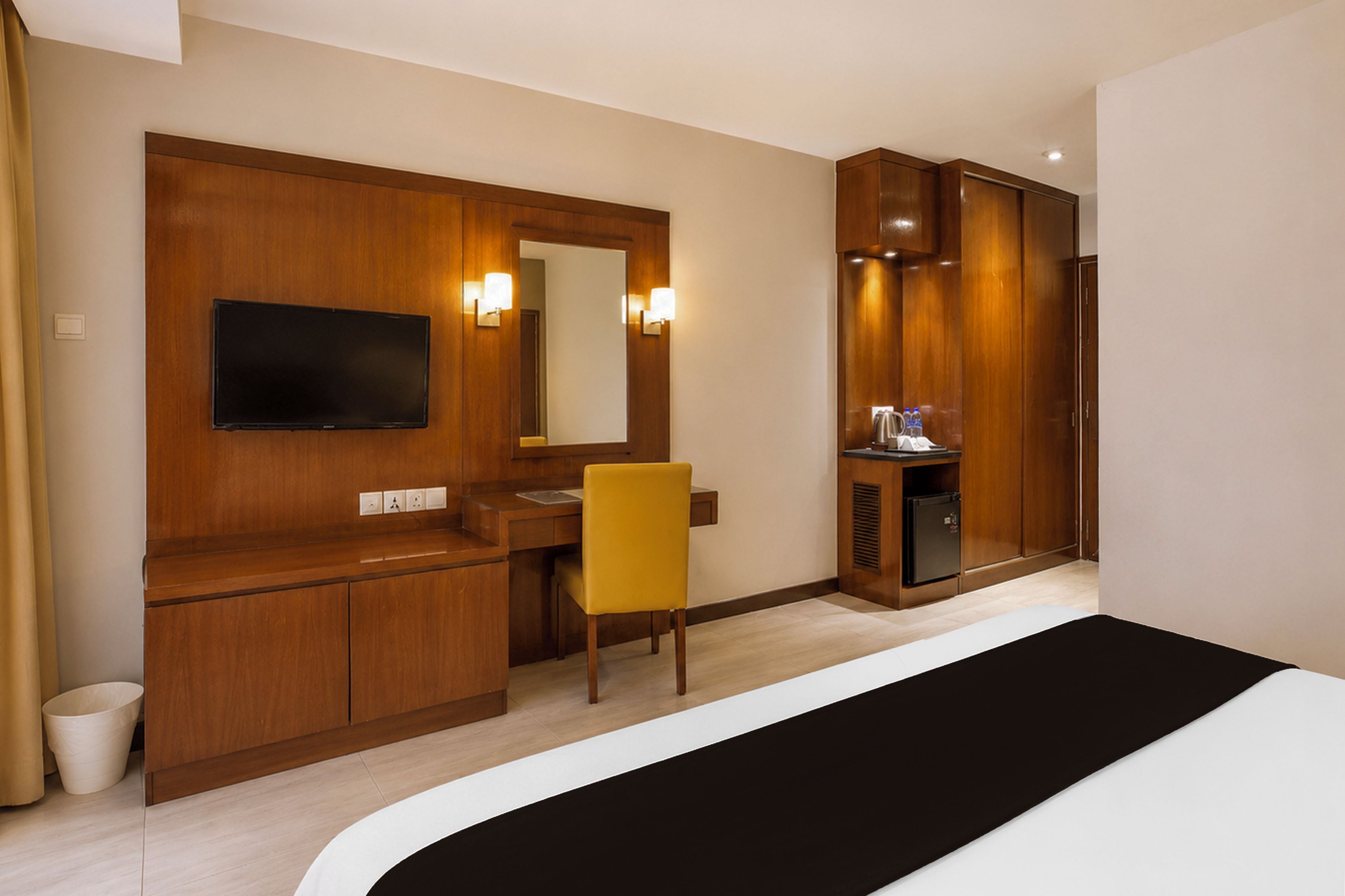 A hotel room with a bed, a desk, a chair, a television, a mirror, and a wardrobe.