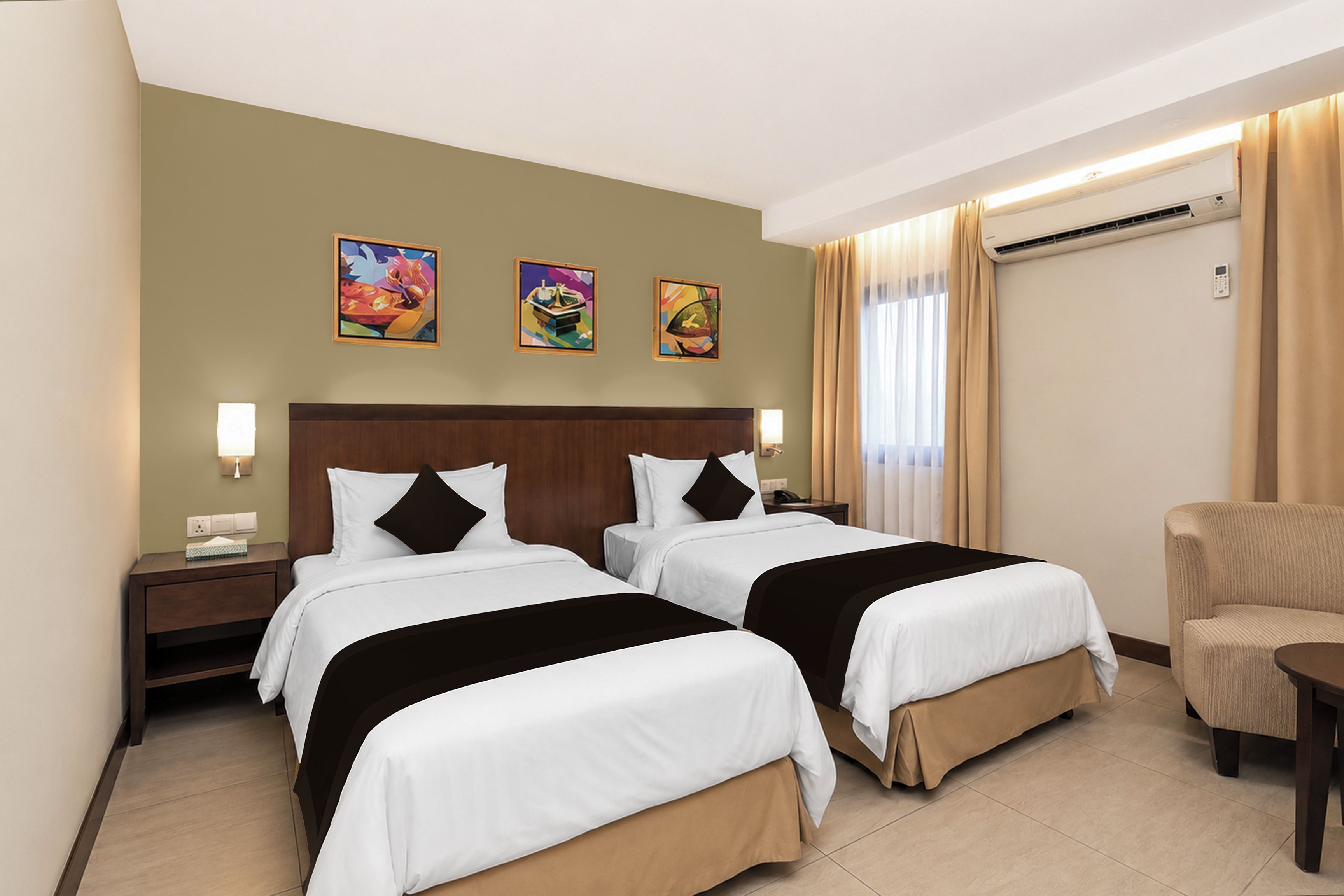 A hotel room with two beds, a desk, a chair, and artwork on the wall.