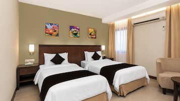 A hotel room with two beds, a desk, a chair, and artwork on the wall.