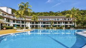A swimming pool with lounge chairs and umbrellas, surrounded by a hotel with multiple floors and balconies.