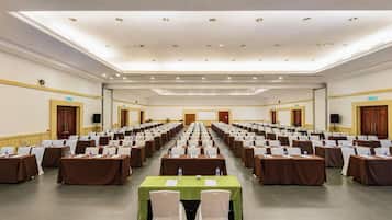 A conference room with rows of tables, chairs, and water bottles, equipped with a projector and speakers.