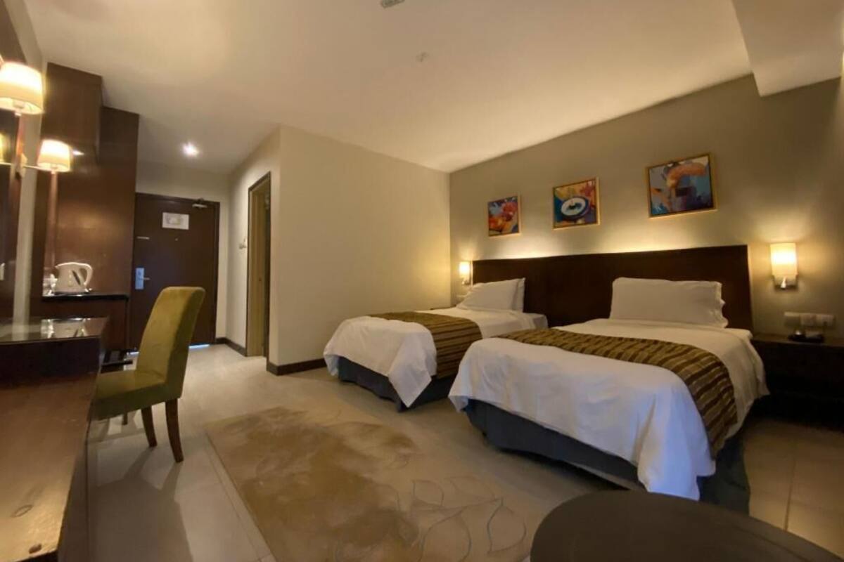 A hotel room with two beds, a desk, a chair, and artwork on the wall.