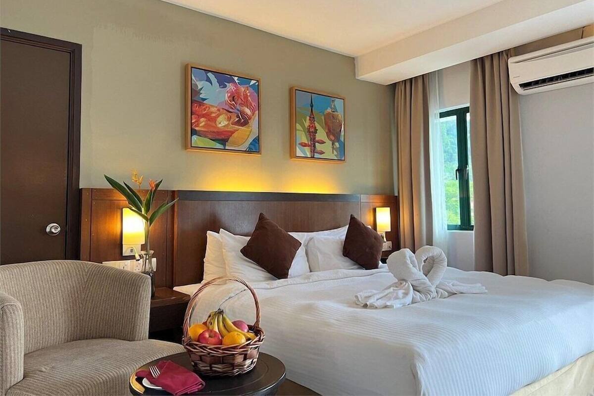 A hotel room with a bed, a chair, a fruit basket, and two paintings on the wall.